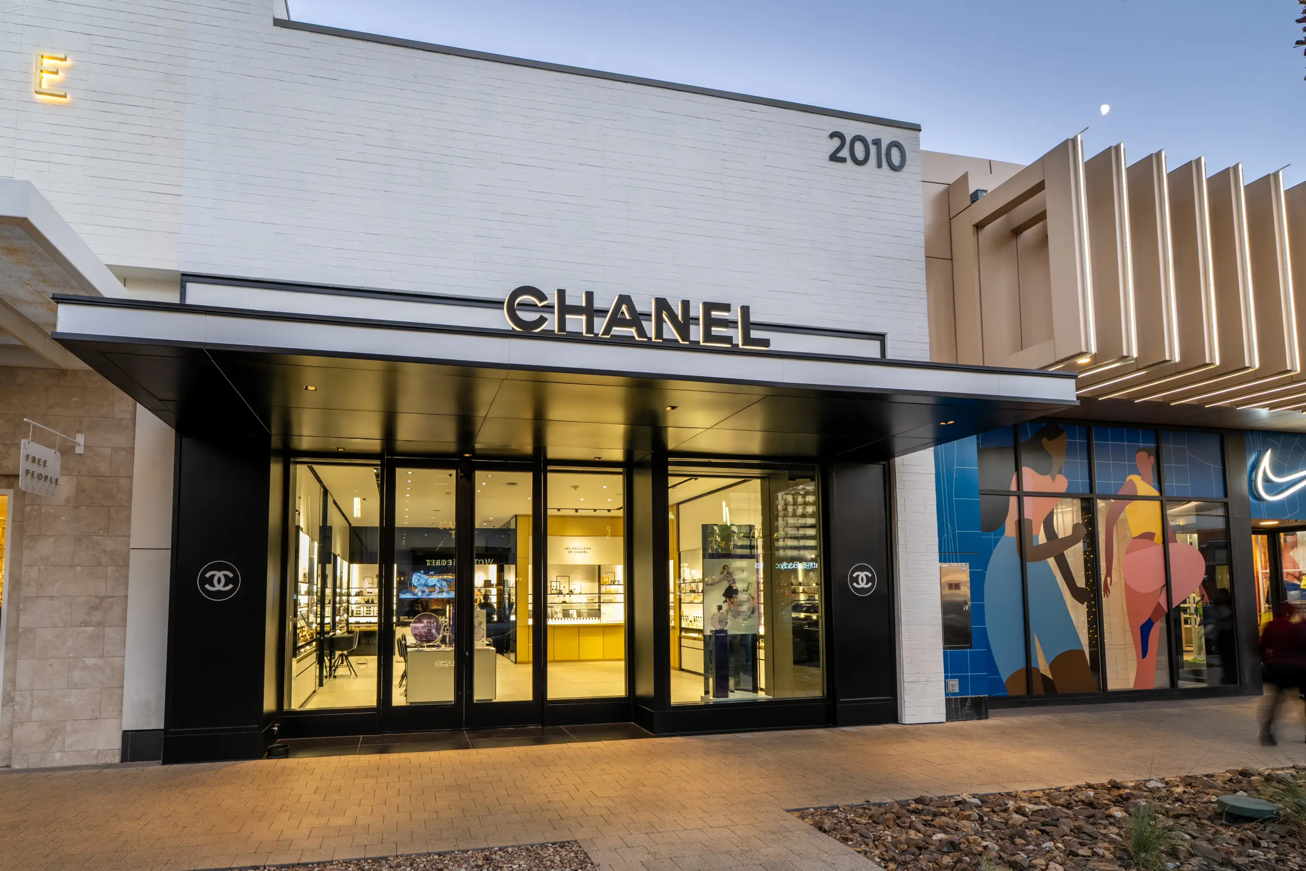 Exterior of a Chanel store with large glass doors and black framing, located at 2010. The storefront is next to a building featuring a colorful mural and a Nike logo. The street and sidewalk are visible in front.