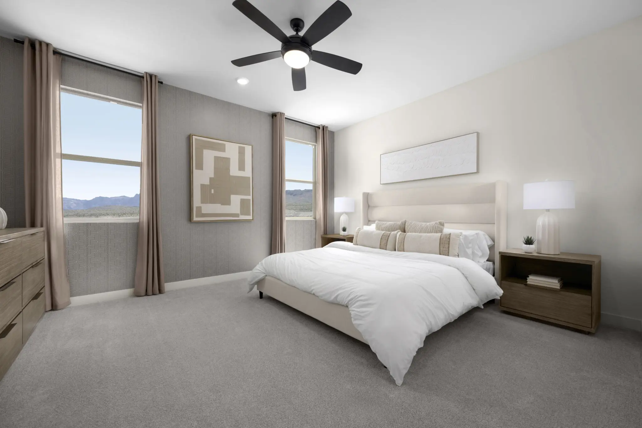 KBLV_LandingsatCaldwellPark_Plan2070-PrimaryBedroom_7508c-11×8-1-2048×1365 Modern bedroom in Plan 2070 at Caldwell Park by KB Home with beige walls, a large bed with white bedding, wooden nightstands and lamps, two big windows with brown curtains, neutral-toned decor, and a sleek black ceiling fan.