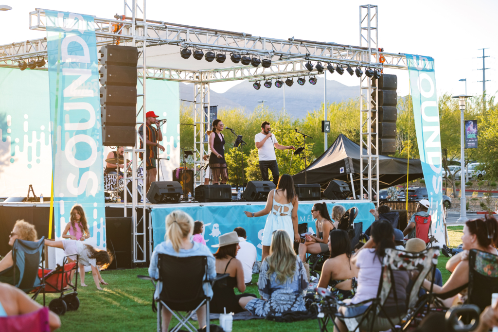 Band performing on stage at Downtown Summerlin’s Summerlin Sounds concert with crowd seated on lawn.