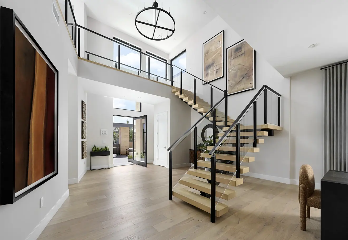 250911_Carlisle_Peak_P3_002 Modern, bright entryway in Plan 3 at Carlisle Peak by Tri Pointe Homes features light wood floors, a floating staircase with glass railing, large windows, abstract art, minimalist decor, and a high ceiling with a black circular chandelier.