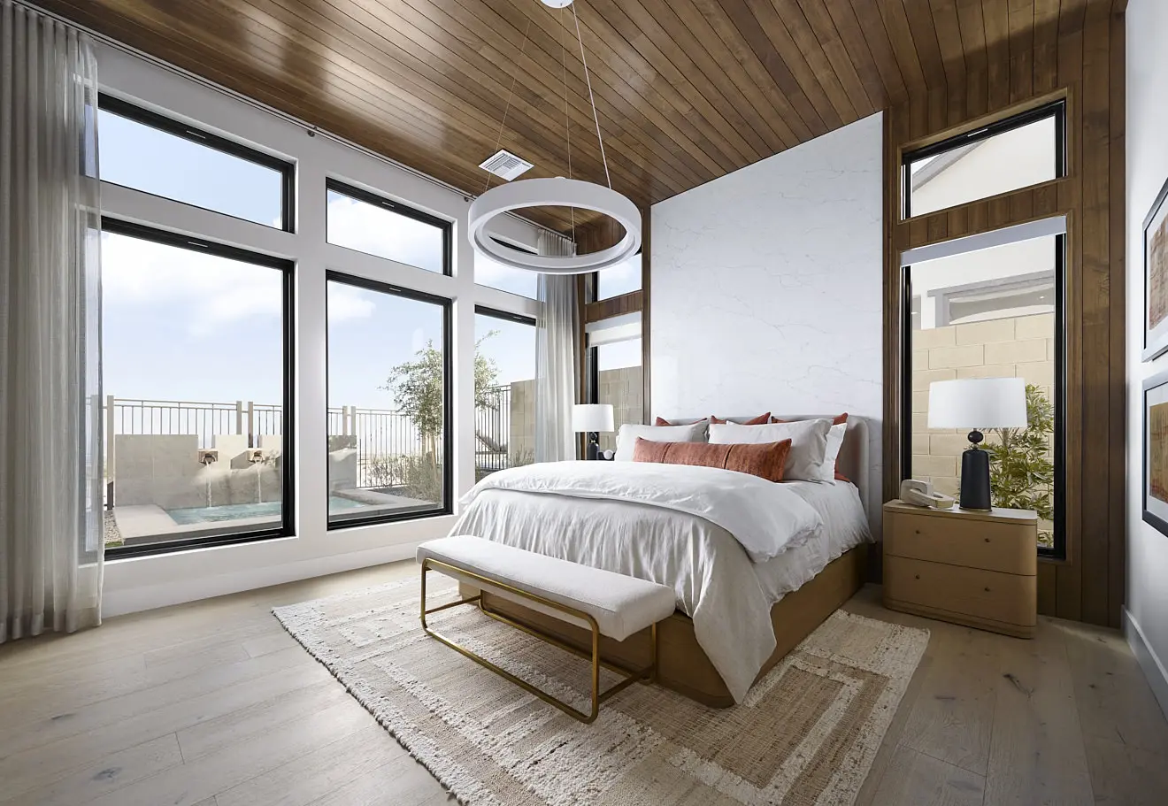 250911_Carlisle_Ridge_P2_005 Modern bedroom at Plan 2 at Carlisle Ridge by Tri Pointe Homes with large windows, a wooden ceiling, white walls, a cozy bed with orange and white pillows, beige bench, nightstands, circular ceiling light, and pool and patio views.