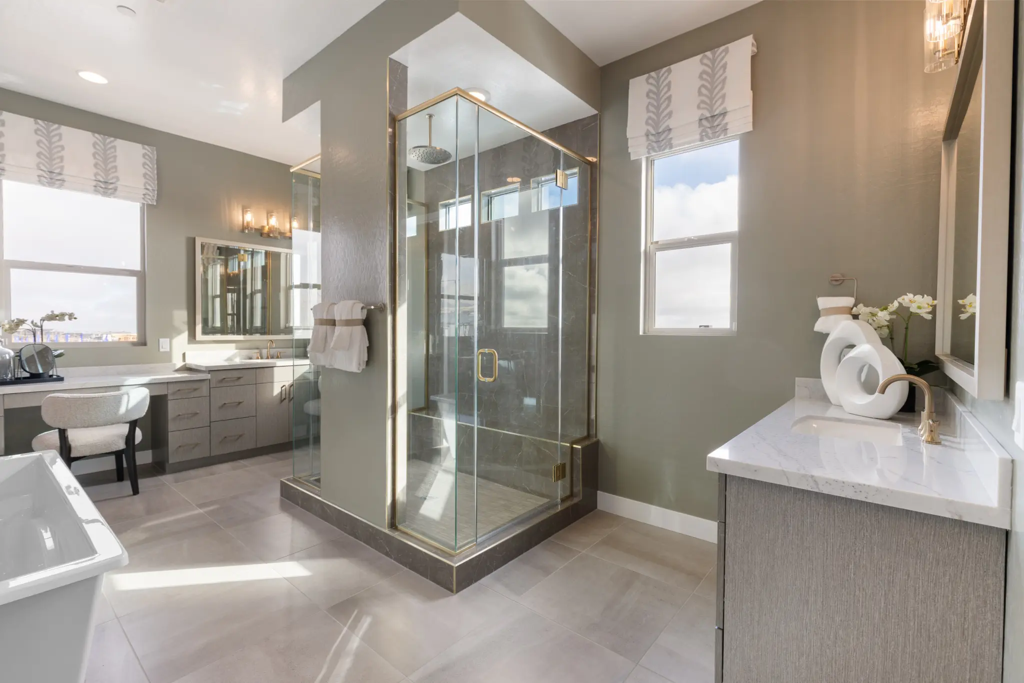 Primrose-Park-Sage-3-2048×1365 Modern bathroom in the Sage II Floorplan at Primrose Park by Richmond American Homes features a glass shower enclosure, bathtub, vanity with mirror, gray walls, large windows with patterned curtains, and light-colored tile flooring.
