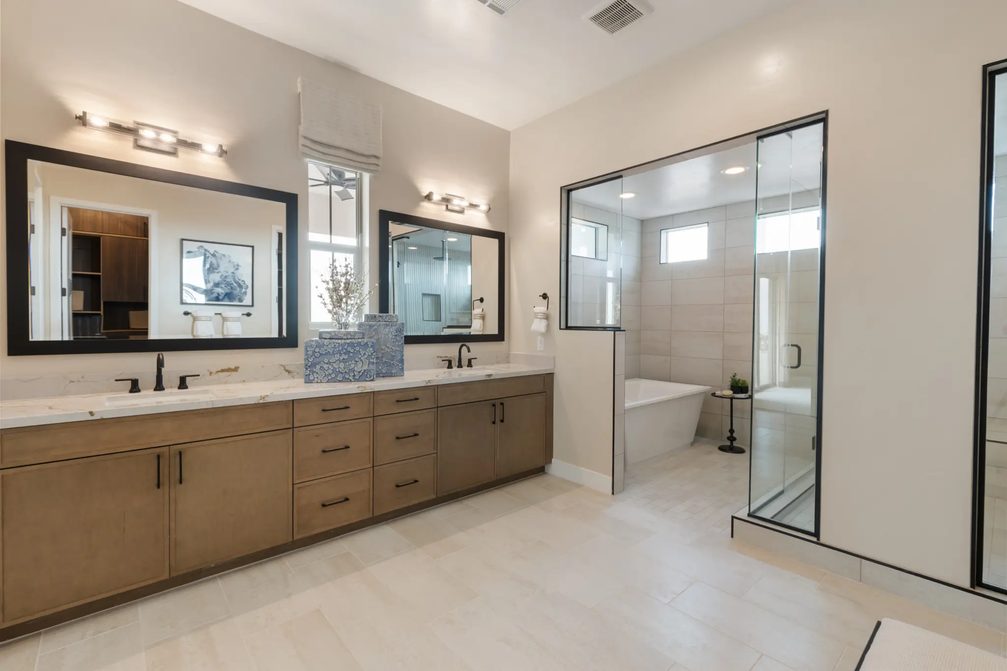 Primrose-Park-Teton-7-2048×1365 Modern bathroom with double sinks, large mirrors, and wooden cabinets in the Teton Floorplan at Primrose Park by Richmond American Homes. A glass-enclosed shower sits beside a bathtub, all enhanced by neutral tones and minimalist decor.
