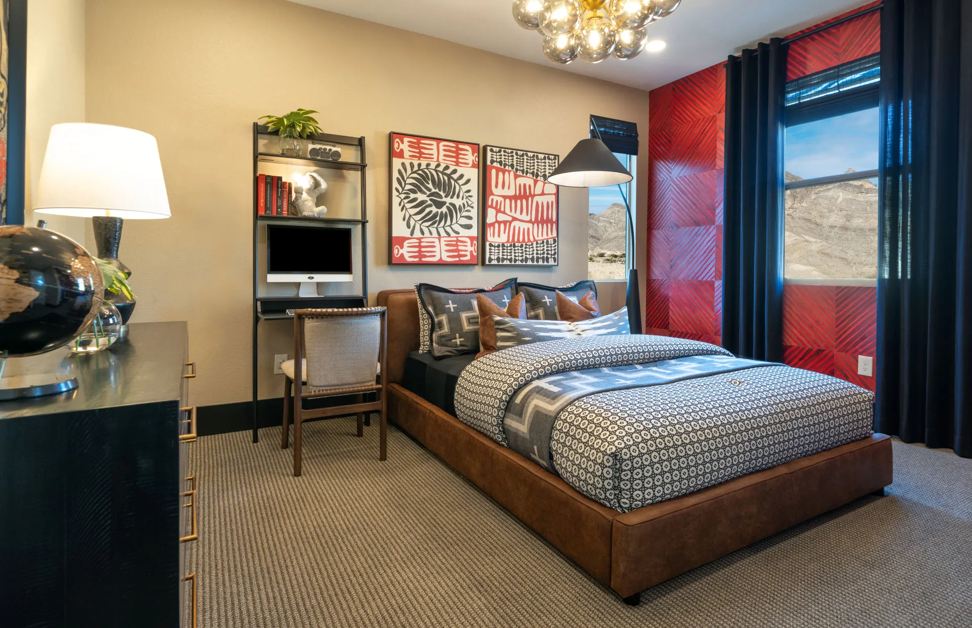 Brantley-Tivoli-Bedroom 4 Modern bedroom at Tivoli at Brantley by Pulte Homes features a brown upholstered bed, geometric bedding, a desk with a computer, bookshelves, contemporary decor, and bold red wall art. Large window offers black curtains and a mountain view.