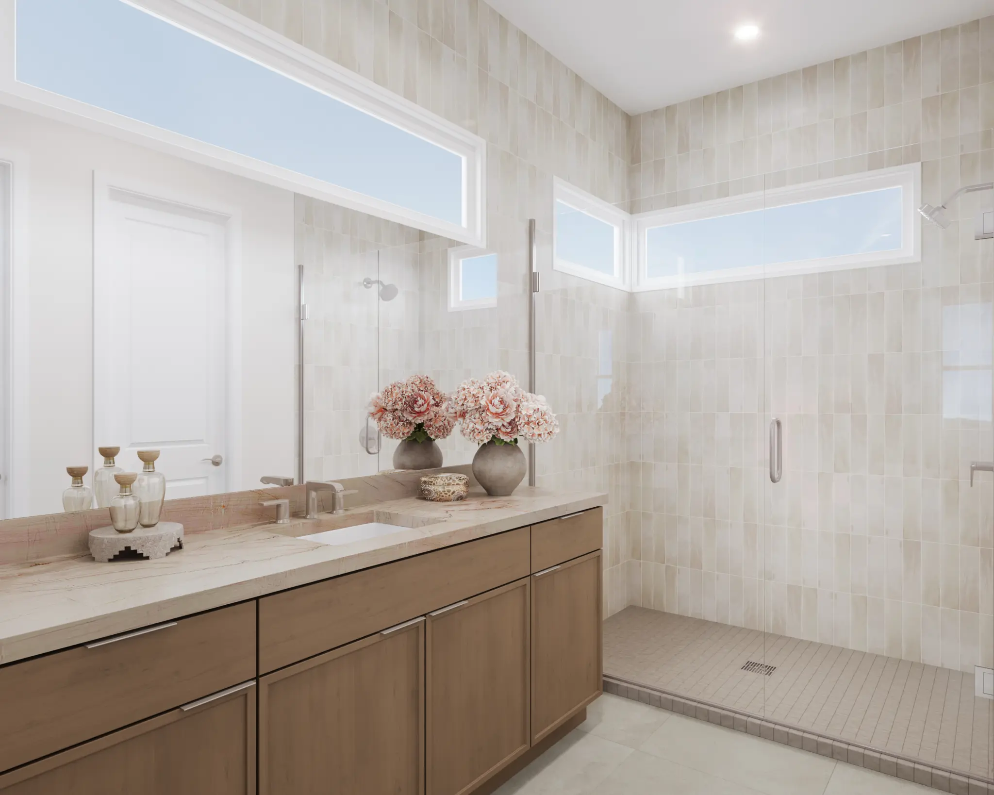 9048_NV-LV_FITZROY_CON_PRIMARY-BATH_1-2048×1638 Modern bathroom in the Fitzroy Floorplan at The Loughton by Toll Brothers features light wood cabinets, a double sink vanity with decorative vases of pink flowers, beige tiled walls, a large mirror, and a spacious glass-enclosed walk-in shower.