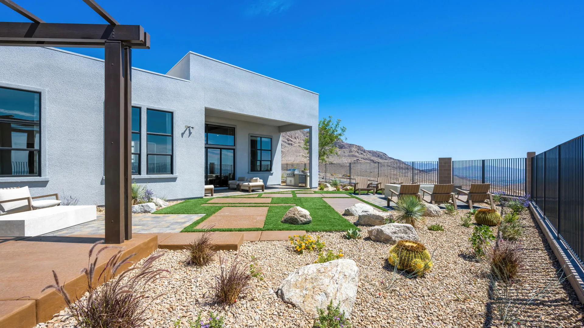 Backyard of Monroe Model at Esplanade at Red Rock by Taylor Morrison (5) Modern backyard with stone landscaping, desert plants, lounge chairs, and a covered patio facing mountains under a clear blue sky.