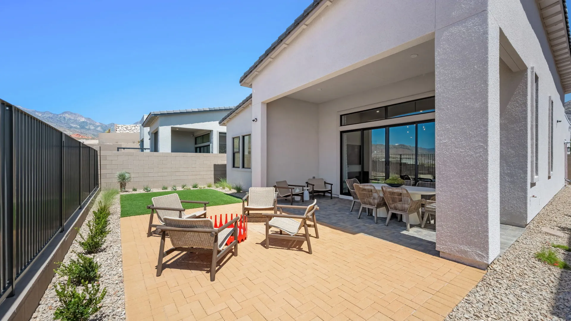 Backyard of Sangria Model at Esplanade at Red Rock by Taylor Morrison (1) Spacious backyard patio with outdoor seating, a game of Connect 4, small grass lawn, modern house exterior, and clear blue sky.