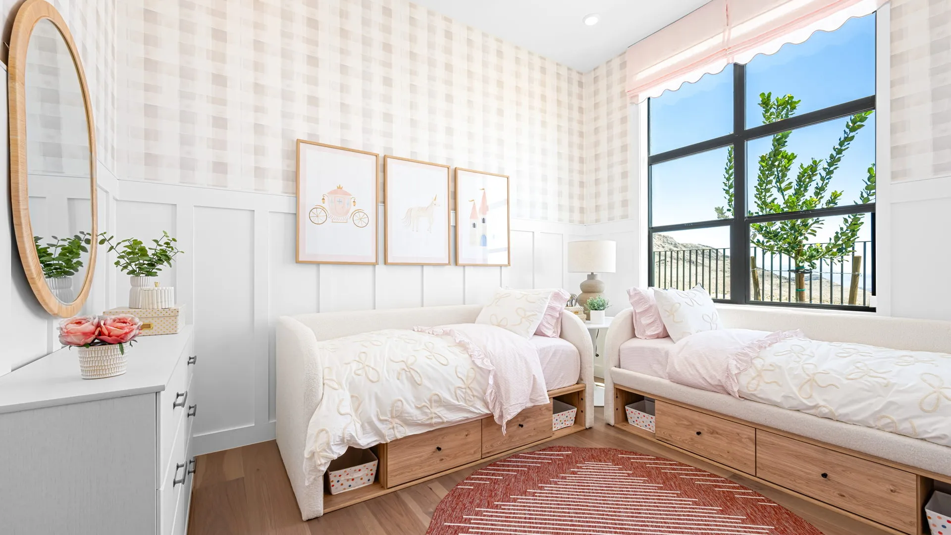 Bedroom of Monroe Model at Esplanade at Red Rock by Taylor Morrison Bright bedroom with two twin beds, light bedding, a round rug, large window, white dresser, and three framed art pieces on the wall. Storage drawers are under each bed. Decor includes flowers and woven baskets.