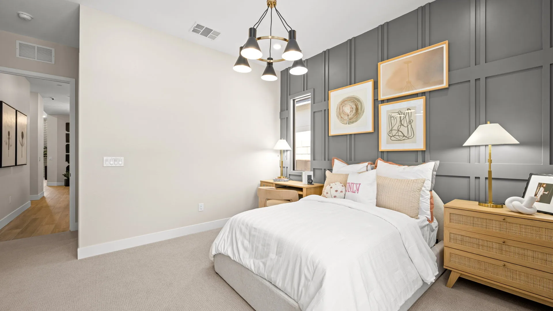 Bedroom of Sangria Model at Esplanade at Red Rock by Taylor Morrison (1) Modern bedroom with a white bed, gray accent wall, framed art, wooden nightstands, a lamp, and ceiling light. Neutral tones and minimal decor create a cozy, inviting atmosphere.