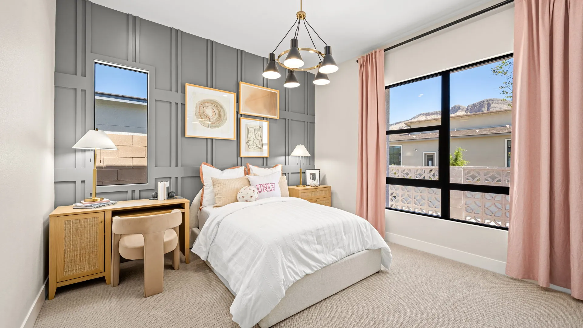 Bedroom of Sangria Model at Esplanade at Red Rock by Taylor Morrison A modern bedroom with a bed, two wooden nightstands, a desk, and pink curtains. The gray accent wall features framed art, and large windows let in natural light.