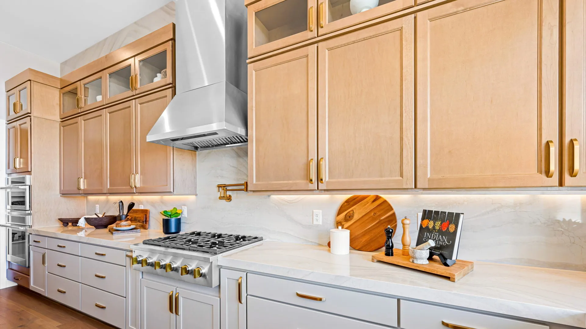 Kitchen of Monroe Model at Esplanade at Red Rock by Taylor Morrison (3) Modern kitchen with light wood cabinets, white countertops, a stainless steel range hood, gas stove, and various kitchen items like utensils, a cutting board, and a cookbook neatly arranged on the countertop.