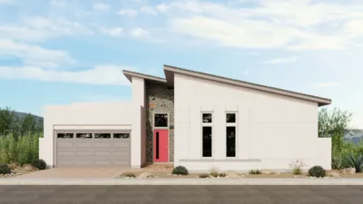 Modern single-story house with a sloped roof, white exterior, stone accent wall, large windows, a double garage, and a red front door. Desert landscaping with small plants and shrubs. Blue sky with scattered clouds.