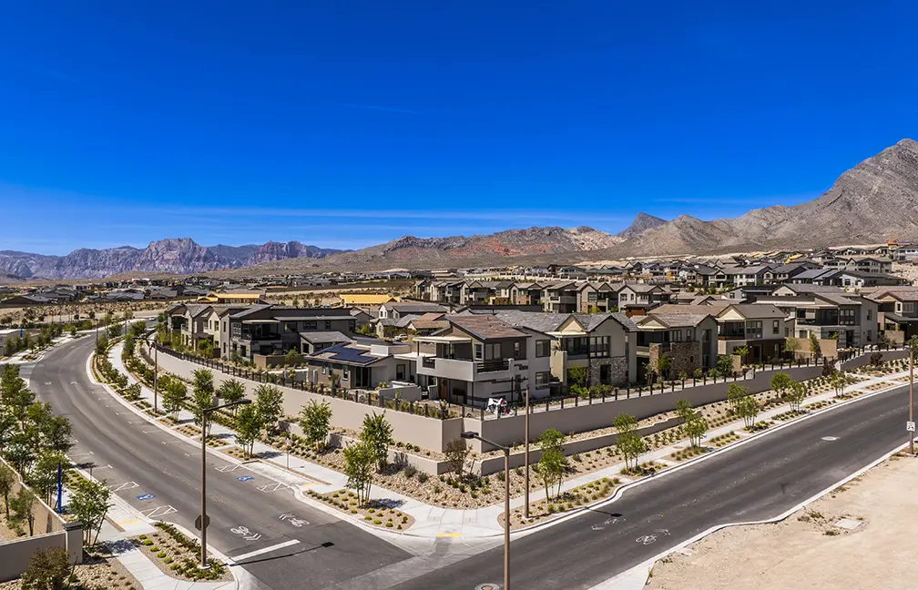 Grand Park Rooftops 05.2026 (1) – SELECT A suburban neighborhood with modern houses, tree-lined streets, and minimal traffic, set against a backdrop of mountains under a clear blue sky. Desert landscaping surrounds the area.