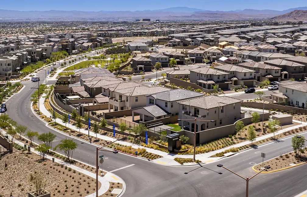 Kestrel Rooftops 05.2026 (5) – SELECT Aerial view of a suburban neighborhood with rows of modern houses, landscaped yards, and curving streets. The area appears dry and is surrounded by mountains in the distance under a clear blue sky.