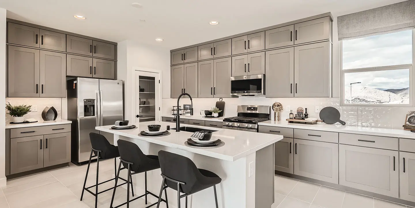 Modern kitchen with light gray cabinets, stainless steel appliances, a large island with a white countertop, three black bar stools, and a window with a mountain view.