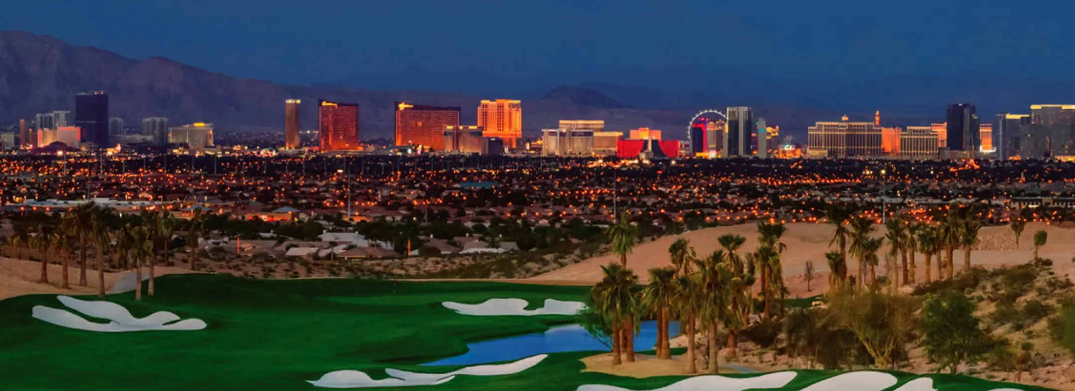 Summerlin_Custom-Summit A lush golf course with sand traps and palm trees in the foreground, overlooking the brightly lit Las Vegas Strip skyline at dusk, with mountains in the background.