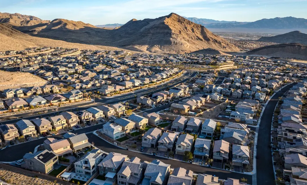 Aerial view of a suburban neighborhood with rows of houses surrounded by desert hills and mountains under a clear sky.