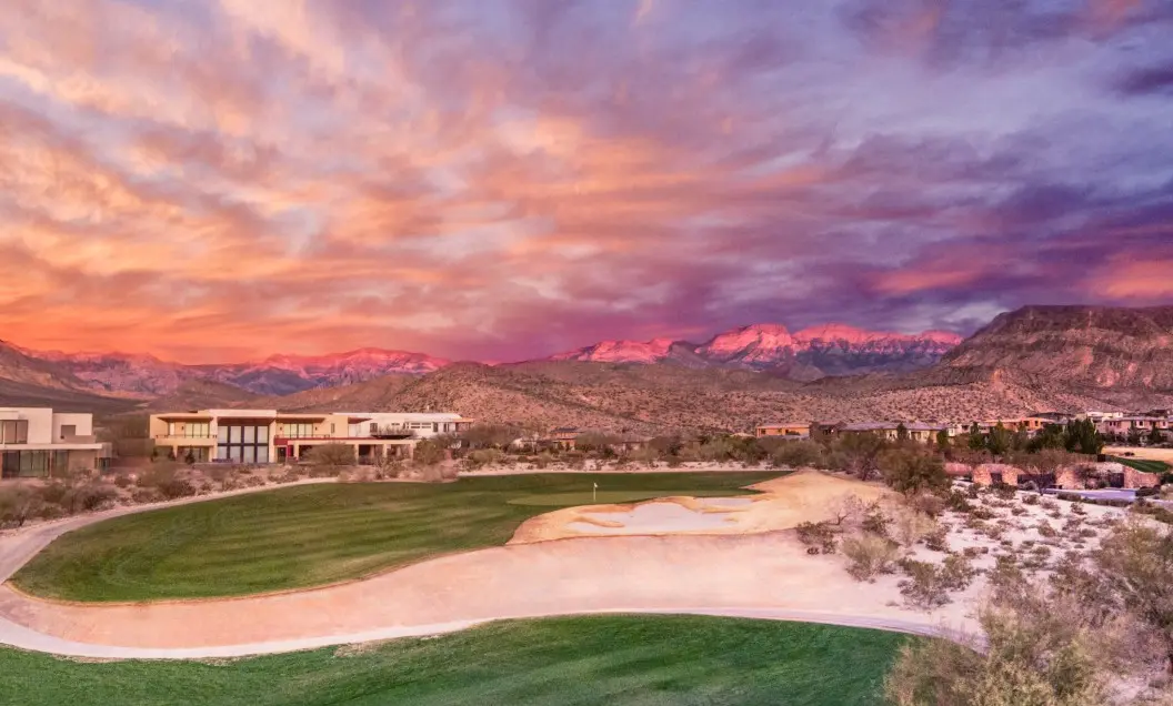 Summerlin_Why-Inspiration A vibrant sunset sky with pink and purple hues over a golf course, desert landscape, and distant mountain range, with buildings visible on the left and right sides of the image.