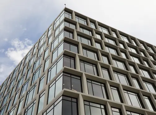 A modern office building with a grid-like facade of rectangular windows, viewed from a low angle against a partly cloudy sky.