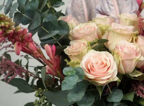 A bouquet featuring pale pink roses, green eucalyptus leaves, and sprigs of small pink flowers, arranged closely together against a light background.