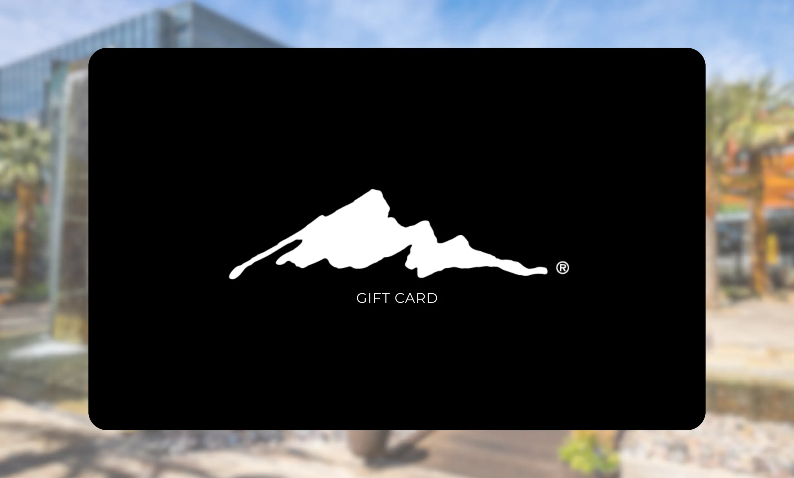A black gift card featuring a white outline of a mountain range in the center, with the words GIFT CARD below the image. The card is shown against a blurred outdoor background.