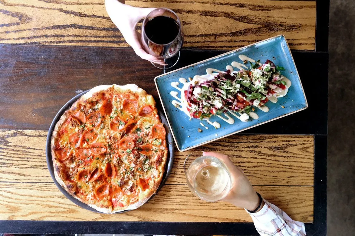 Friends sharing a Pepperoni pizza and appetizer with wine at Public School 702 in Downtown Summerlin