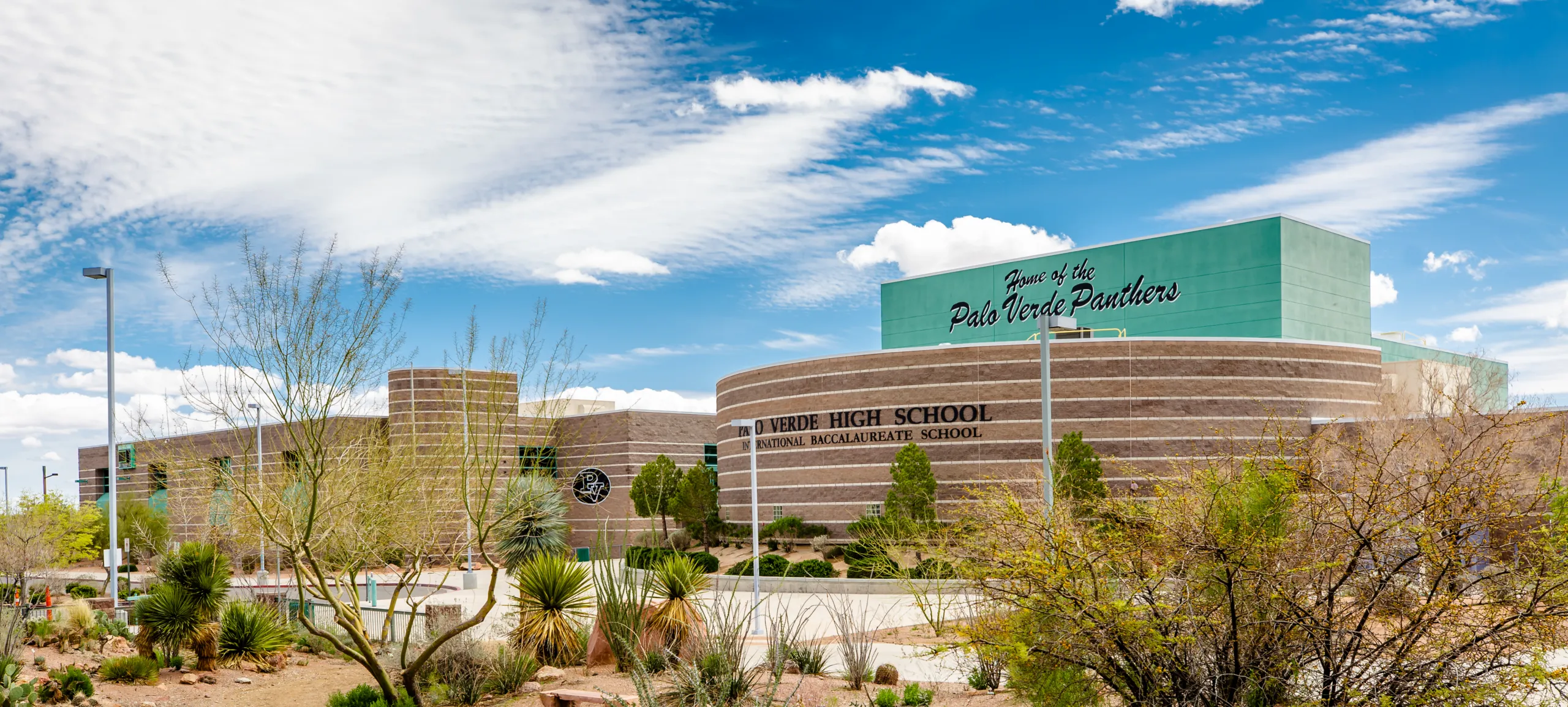 A modern high school building with a sign reading Home of the Palo Verde Panthers and desert landscaping in front, set under a partly cloudy blue sky.