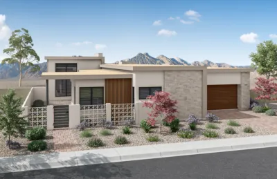 Modern single-story house with a flat roof, stone and wood accents, large windows, and a garage. Desert landscaping with rocks, shrubs, and small trees. Mountains are visible in the background under a blue sky.