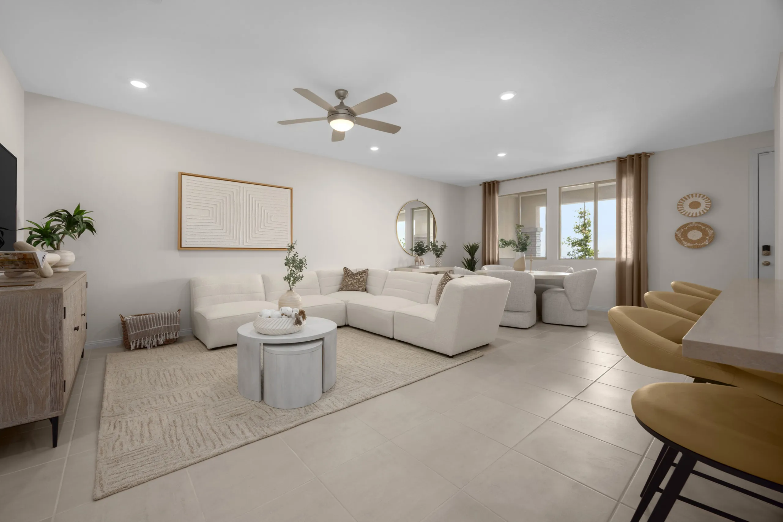 Modern living room with a white sectional sofa, round coffee tables, neutral decor, bar stools at a counter, and large windows letting in natural light.