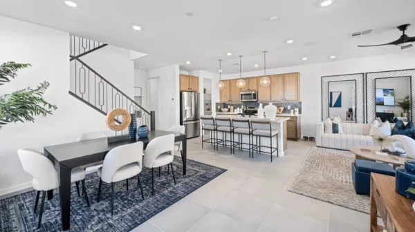 Modern open-concept living space with dining area, kitchen with island seating, and living room. Light wood cabinets, stainless appliances, and neutral tones create an airy, inviting atmosphere.