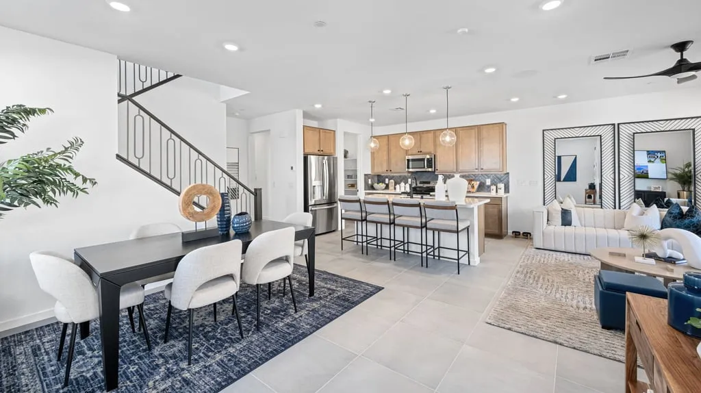 Modern open-concept living space with dining area, kitchen with island seating, and living room. Light wood cabinets, stainless appliances, and neutral tones create an airy, inviting atmosphere.