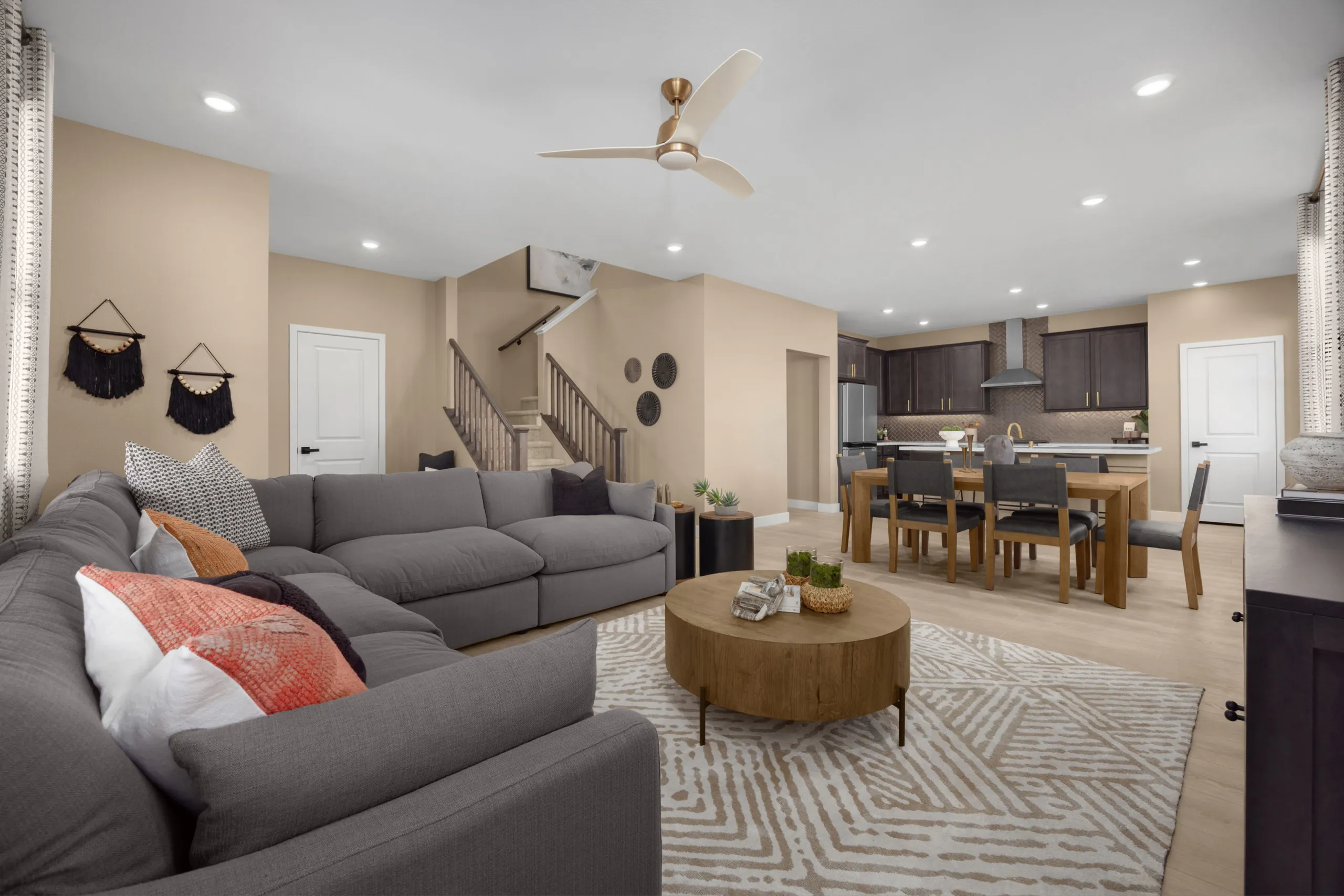 Open-concept living room featuring a large grey sectional sofa, a round wooden coffee table, and a dining area with a wooden table and chairs.